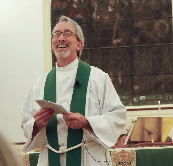 Fr. Chuck Weiss, smiling, in white vestments and a green stole